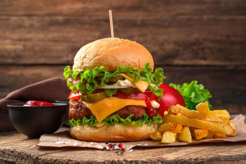 Meat burger with cheese, vegetables, French fries on a wooden background.